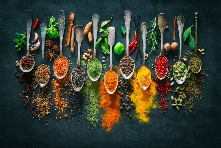 A flat lay of spices in small bowls, including cumin, turmeric, coriander, and garam masala, with a traditional Pakistani vibe.